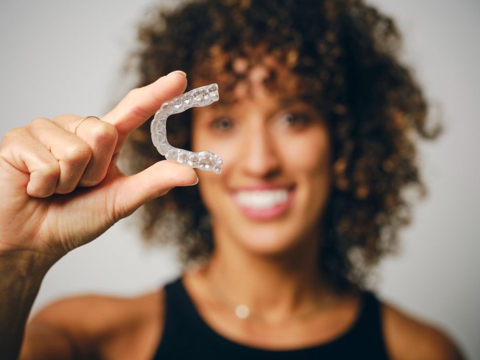 A smiling woman holding an invisible mouthguard