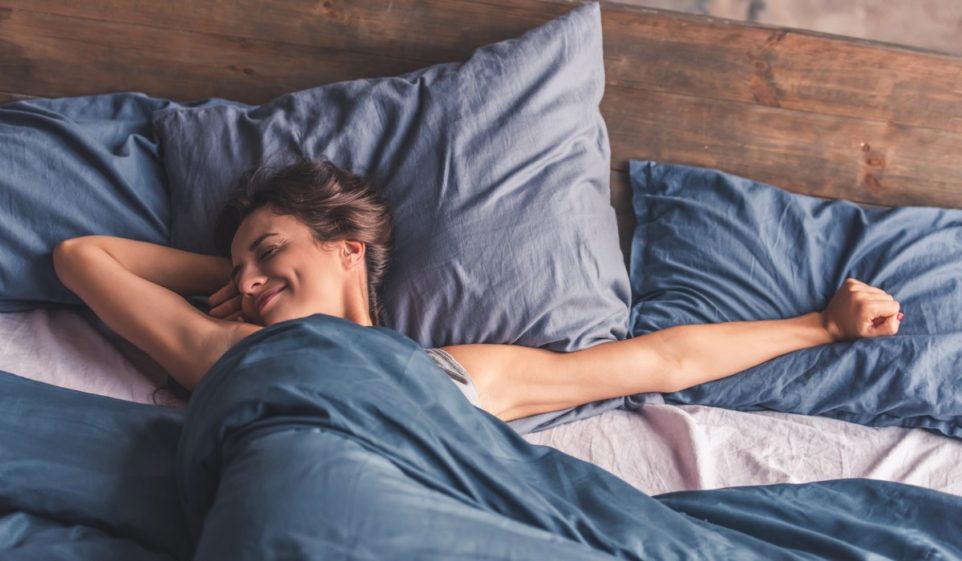 Beautiful young woman is stretching and smiling while lying in bed in the morning