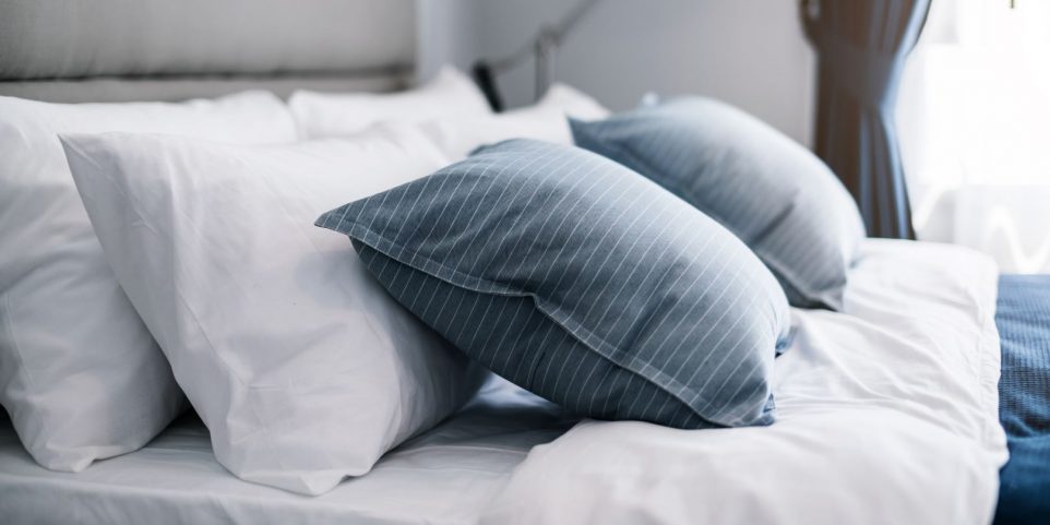 Bed maid-up with clean white pillows and bed sheets in beauty room. Close-up. Lens flair in sunlight.